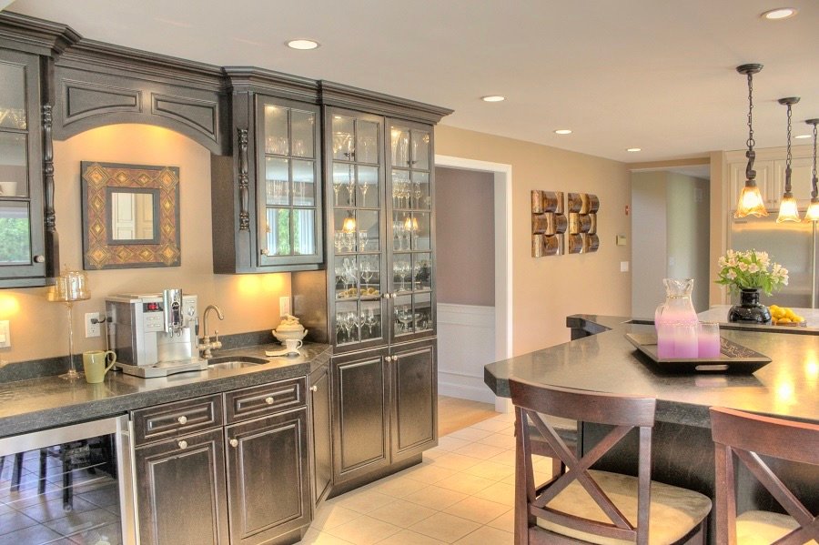 This elegant ornate kitchen features glass cabinets, a beverage fridge, island seating and hanging pendant lights 